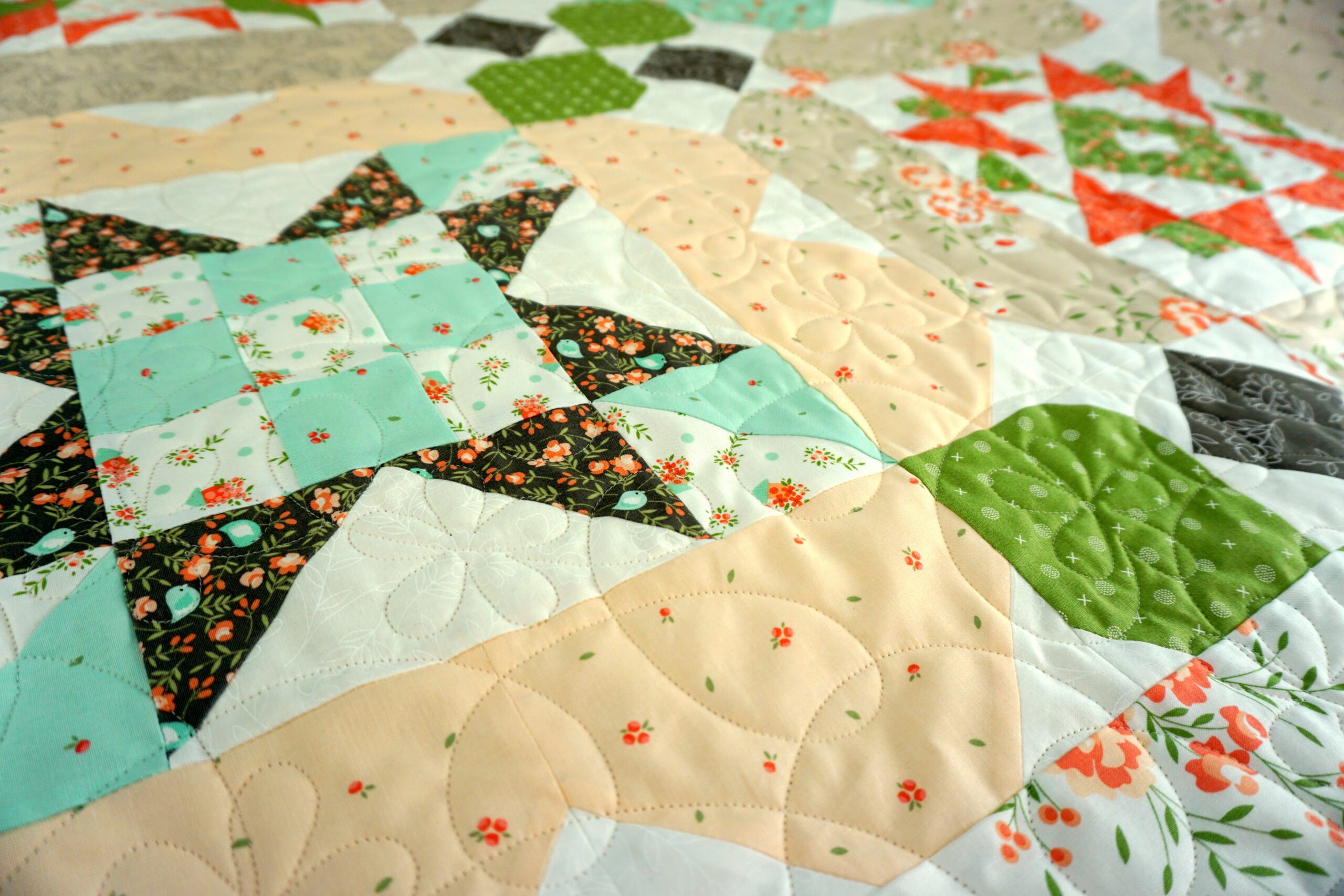 Close-up of Ragtime Flowers pantograph quilted in cream thread over coral and aqua star blocks